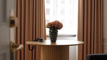 Ein Zimmer mit einem Holztisch, einem Blumenstrauß in einer Vase und einem Vorhangfenster.