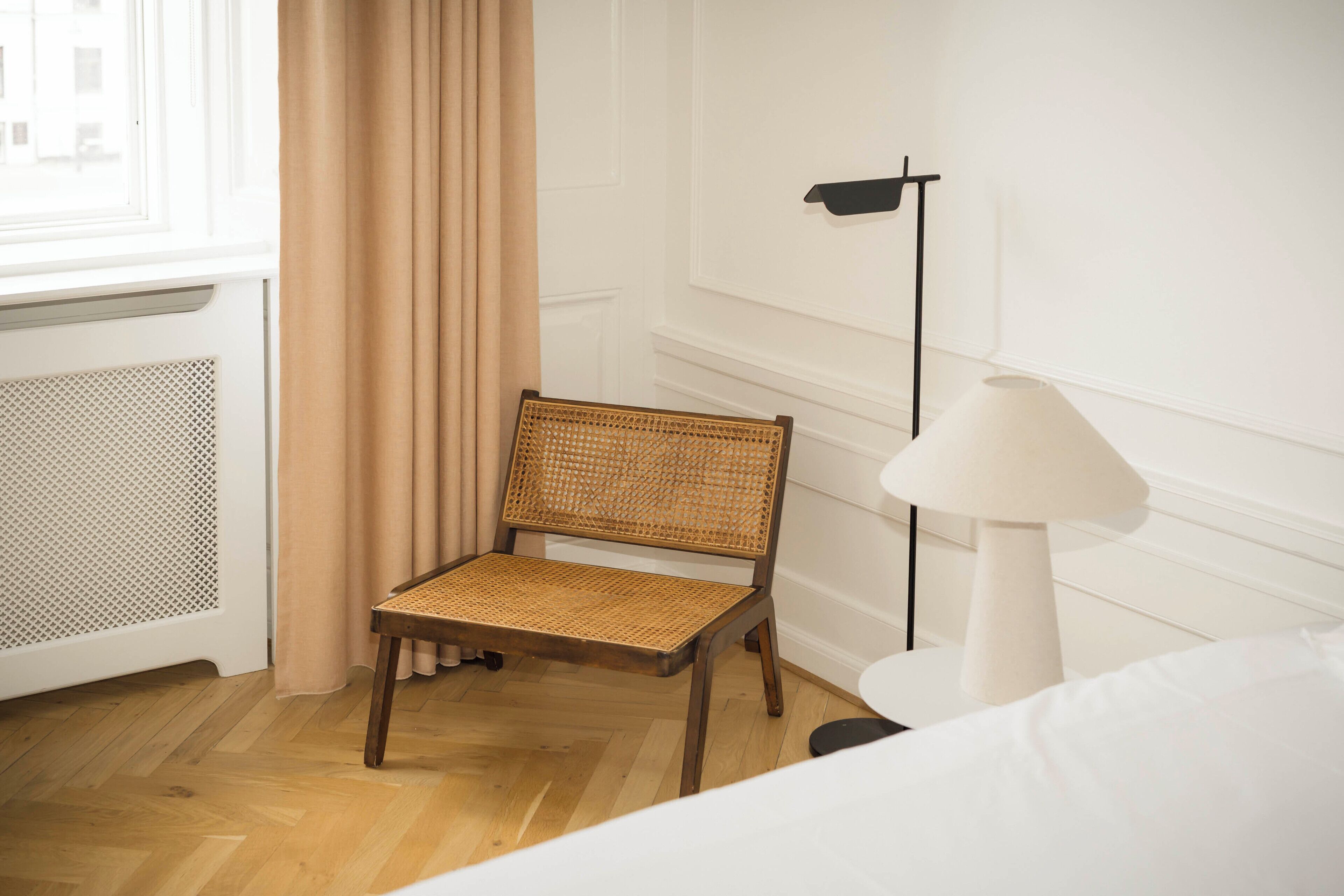 A room with a wooden chair, a white lamp, and a bed.