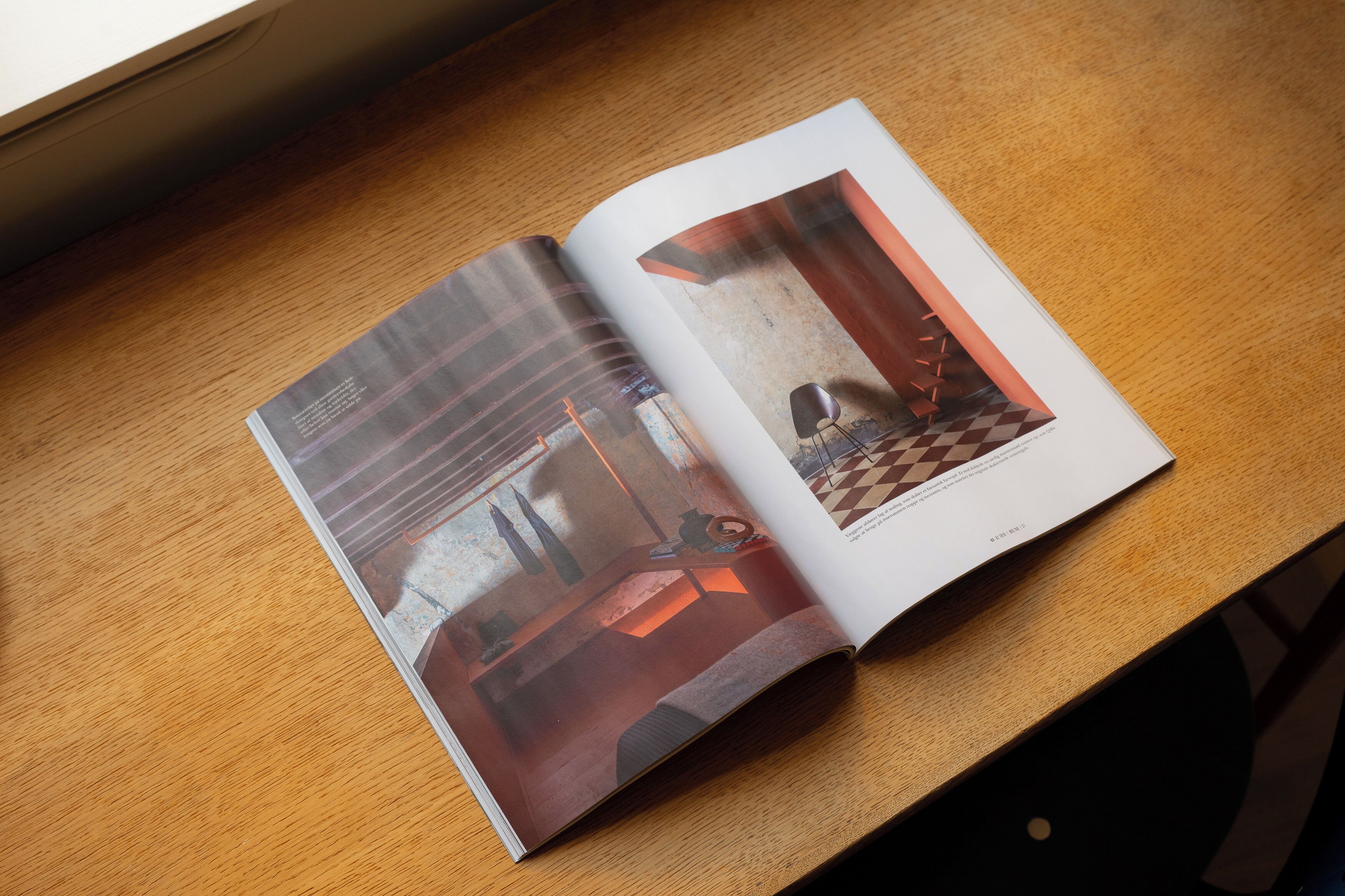 An open magazine on a wooden table, featuring a room with a checkered floor, a lamp, and a chair.
