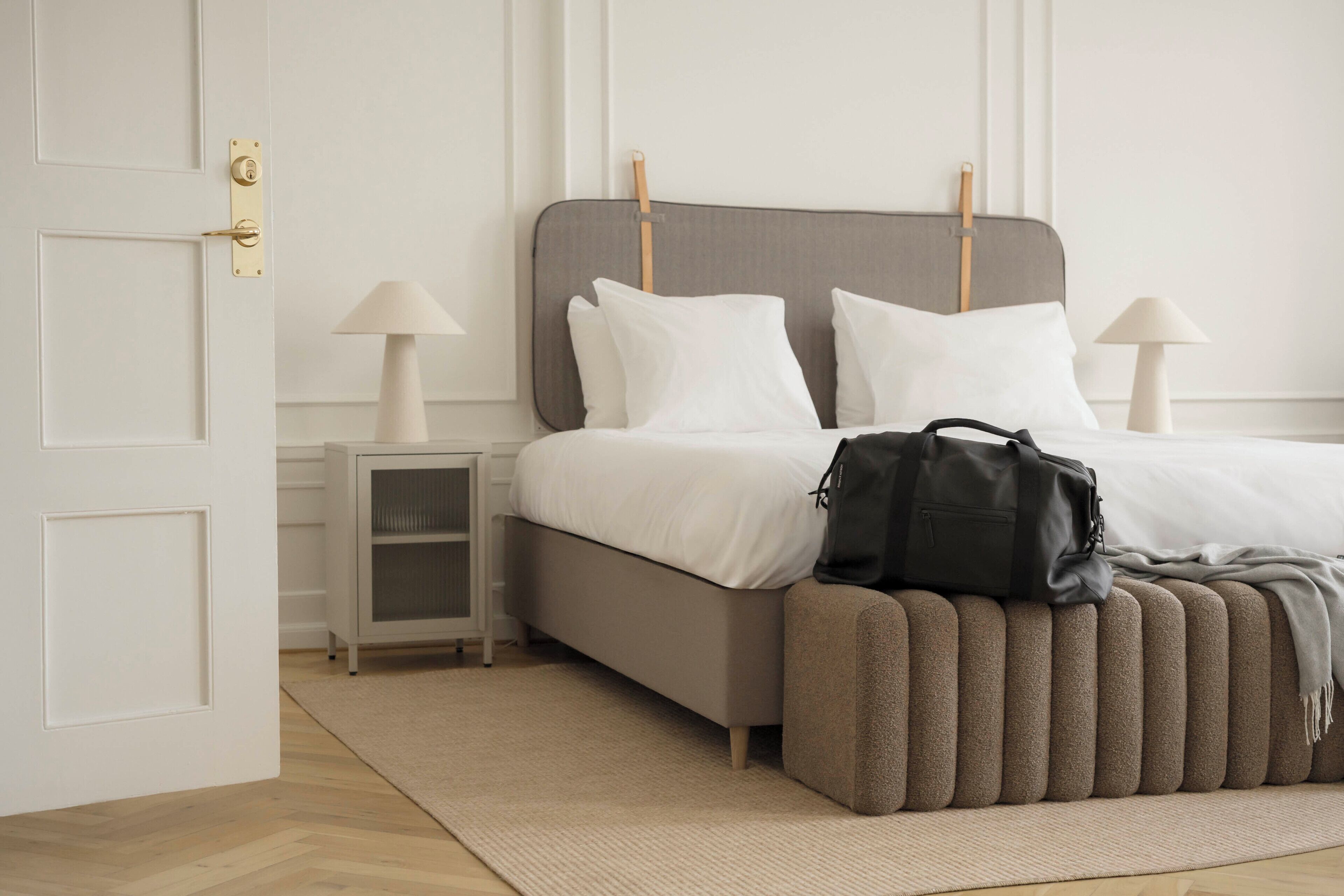 Un dormitorio con cama, mesitas de noche, un banco y una puerta.