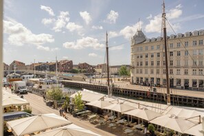 Ett kafé vid floden med uteservering, utsikt över floden och en stor byggnad med klassisk arkitektur i bakgrunden.