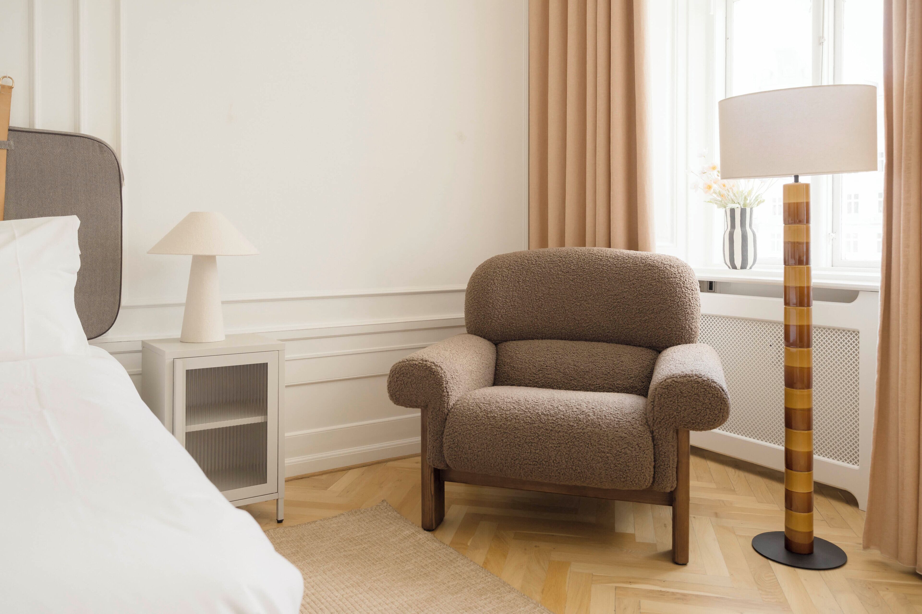 Una habitación de hotel con cama, una silla, una lámpara y un ventanal con cortinas.