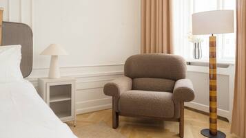 Una habitación de hotel con cama, una silla, una lámpara y un ventanal con cortinas.