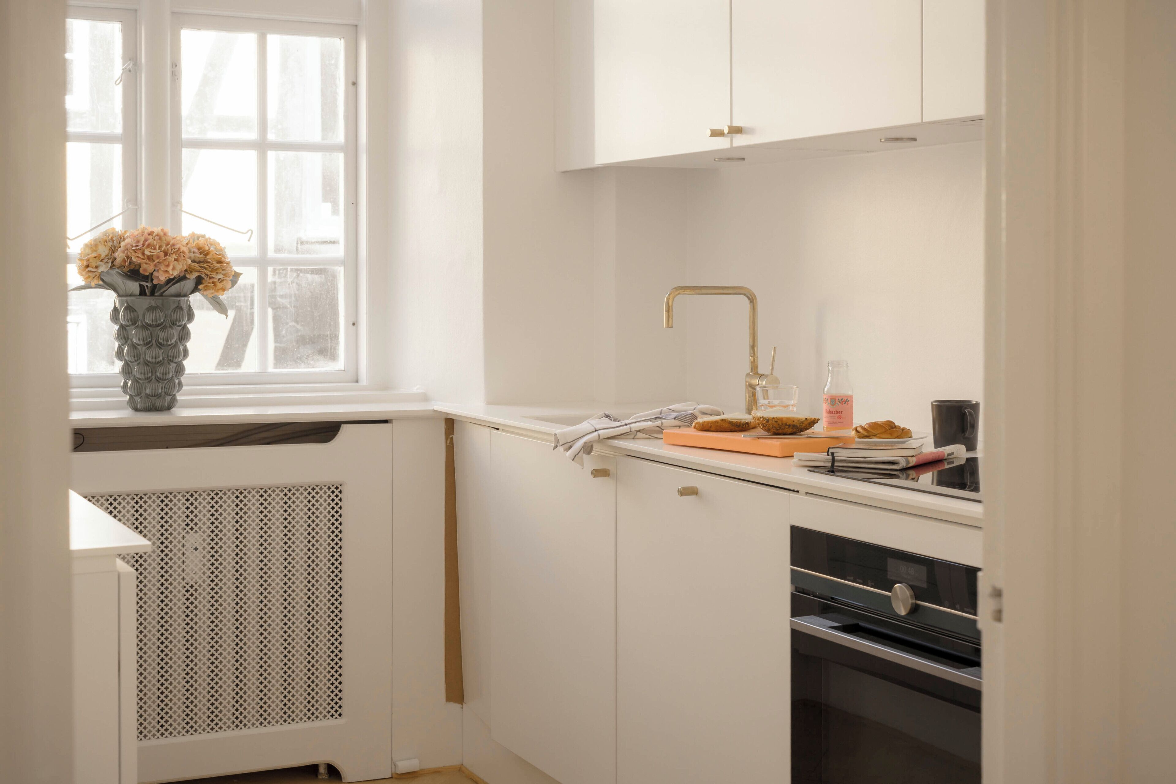 A kitchen with white cabinets, a window, a sink with a gold faucet, and a vase with flowers on the counter.