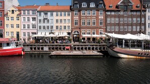 Un canal con barcos amarrados, una hilera de edificios coloridos y un puente con gente caminando.