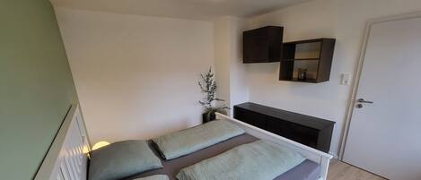 A single bed with a headboard, a bedside table with a lamp, a wall-mounted TV, and a door.