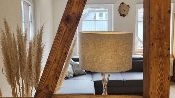 Een kamer met houten balken, een bank, een lamp en een wandklok.