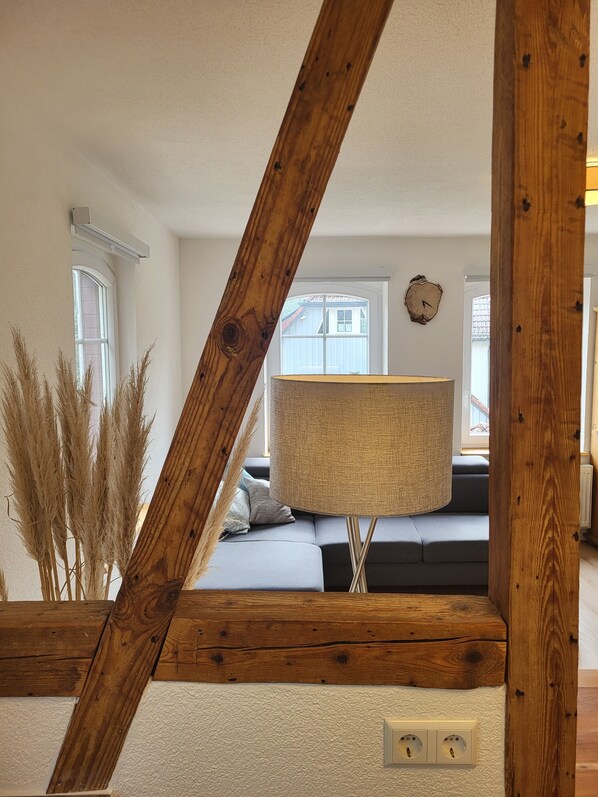 A room with a wooden beam structure, a sofa, a lamp, and a wall clock.