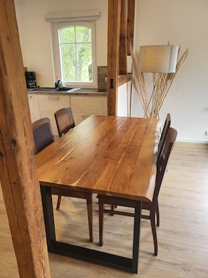 Ein Holzespeisetisch mit Stühlen, ein Fenster mit Blick auf Grünflächen und eine Lampe mit Trockenpflanzen.