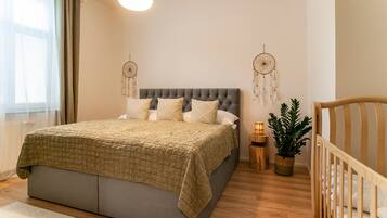 Un dormitorio con cama, mesitas de noche, una cuna, una lámpara colgante y dos atrapasueños.