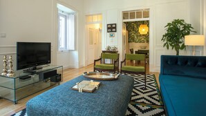 A modern living room with a flat-screen TV, a glass coffee table, a blue sofa, and a patterned rug. - Portas de São Bento Apartment (Lisbon)