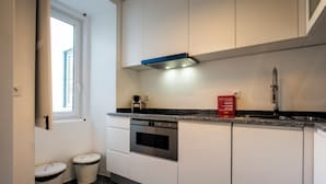 A modern kitchen with white cabinets, a built-in oven, a stainless steel sink, and a window providing natural light. - Portas de São Bento Apartment (Lisbon)
