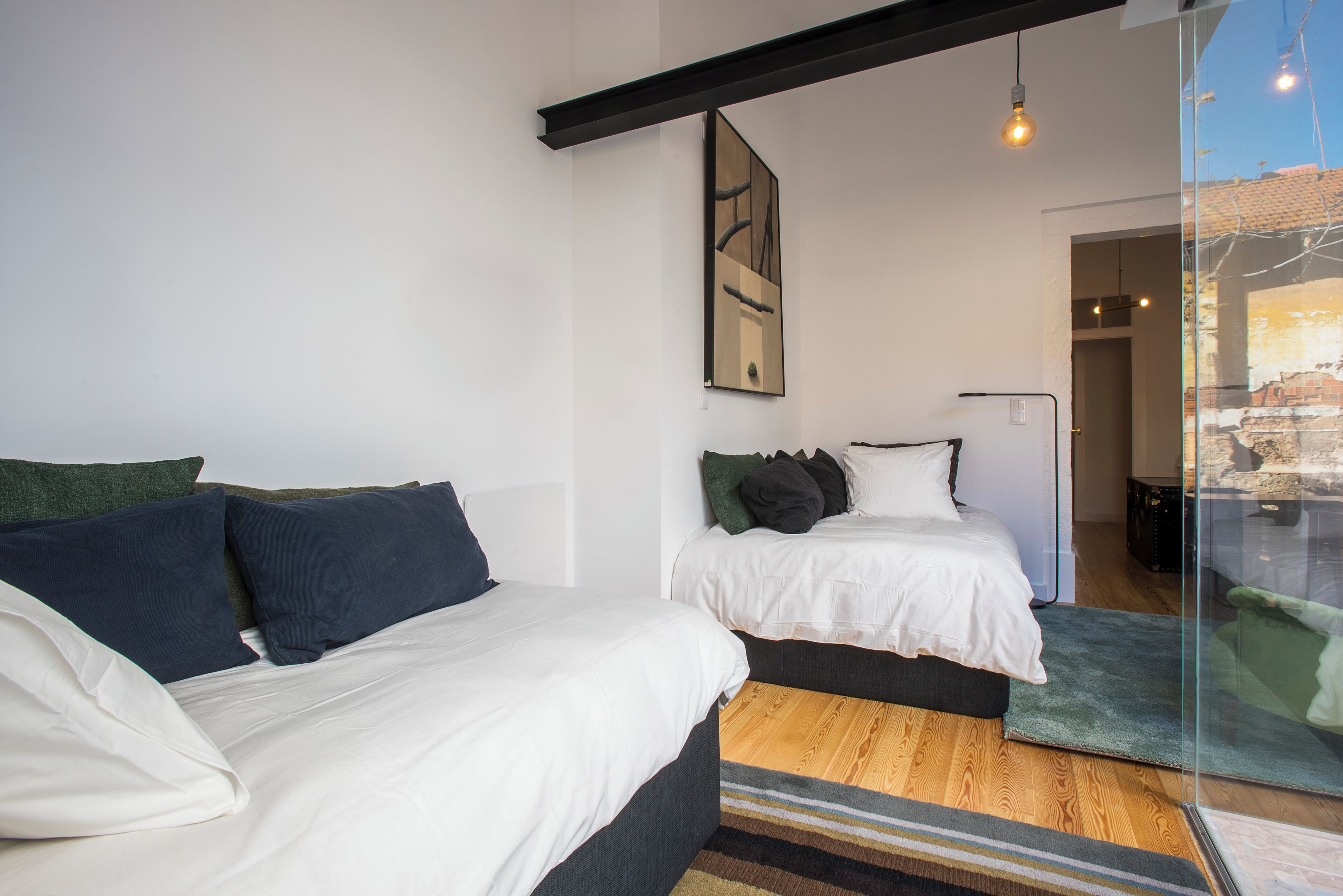 A modern bedroom with two beds, a large window, and a view of the city.