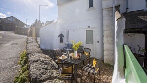 Un pequeño espacio al aire libre con una mesa y sillas, una pared blanca y una valla verde.