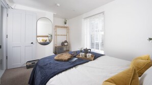 Un dormitorio con cama, espejo, ventana con persianas, puerta y un estante con objetos.