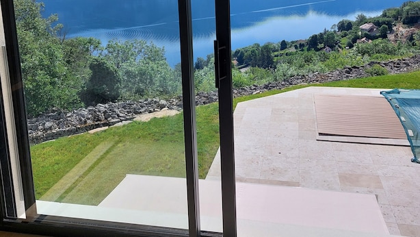 Une pièce dotée d’une grande porte-fenêtre coulissante donnant sur un balcon avec vue sur un lac et des montagnes.