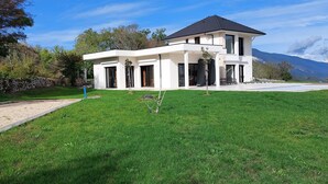 Une maison moderne à deux étages, dotée d’une grande pelouse à l’avant et surplombant un paysage montagneux.