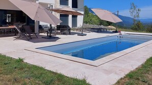 Une maison moderne dotée d’une piscine, de mobilier d’extérieur et de parasols.