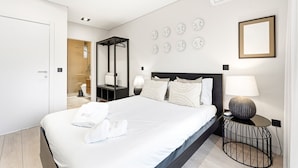 A modern hotel room with a large bed, a bedside table with a lamp, a wall-mounted mirror, and a framed picture. - GuestReady - Quental Wallpaper near Marquês Square (Porto)