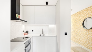 A compact kitchen with white cabinetry, a built-in oven, and a stainless steel sink. - GuestReady - Quental Wallpaper near Marquês Square (Porto)