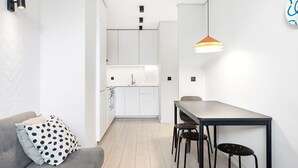 A modern interior with a grey sofa, a dining table with four chairs, a kitchen area, and a pendant light. - GuestReady - Quental Wallpaper near Marquês Square (Porto)