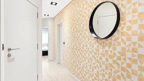 A hallway with patterned walls, a round mirror, and a door leading to a bedroom. - GuestReady - Quental Wallpaper near Marquês Square (Porto)