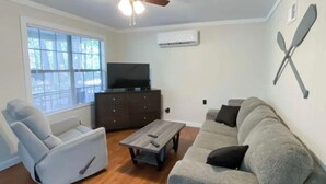 Un salon avec un ventilateur de plafond, un canapé gris, un fauteuil inclinable, une table basse et un téléviseur.