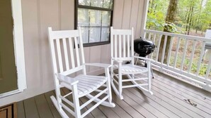 Une véranda avec deux fauteuils à bascule blancs et un barbecue.