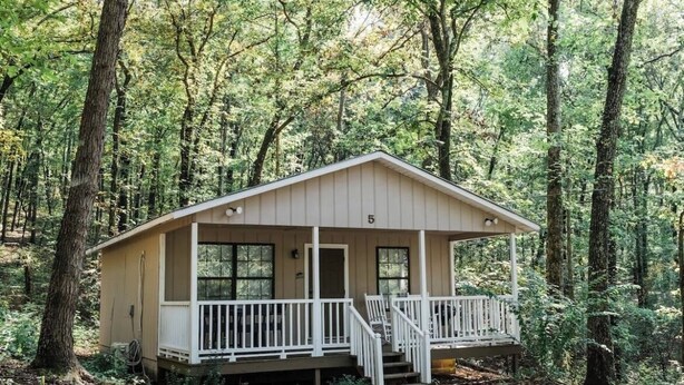 Une petite cabane dotée d’un porche, entourée d’arbres.