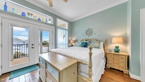 A bedroom with a bed, dresser, nightstands, and a view of the outside. - Blue Turtle Beach House (Panama City Beach)