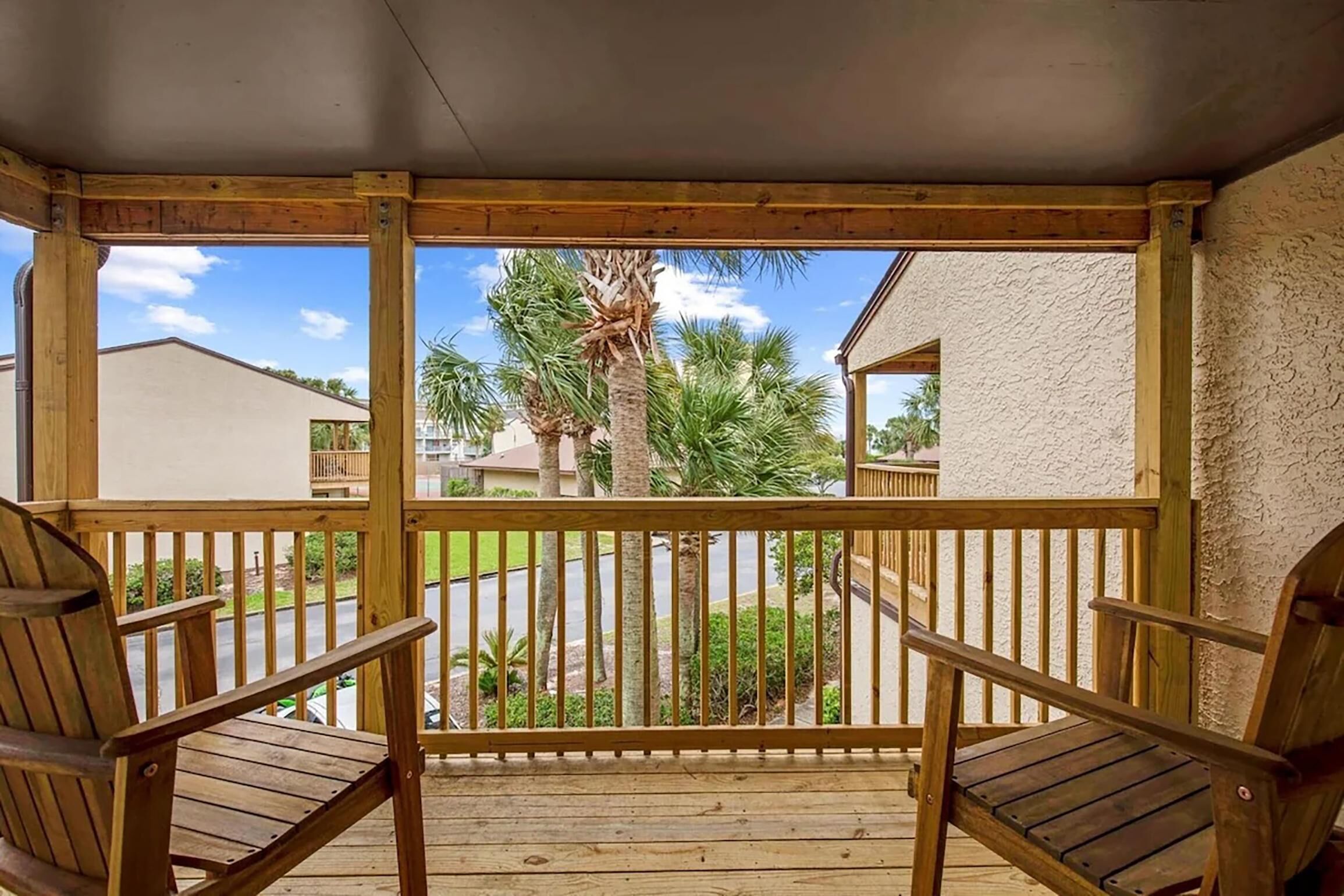 Un pontile in legno con due sedie e una ringhiera, affacciato su una zona residenziale con palme e case.
