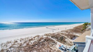 Blick auf einen Strand vom Balkon aus, mit blauem Himmel, Sandstrand und Dünen.