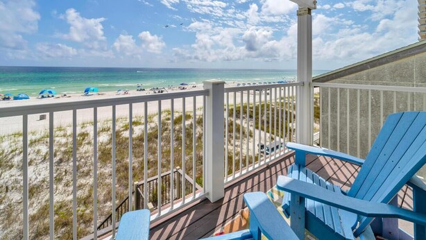Blick auf den Strand von einer überdachten Terrasse mit blauen Stühlen, einer Geländer und der Aussicht auf Ozean und Strand.