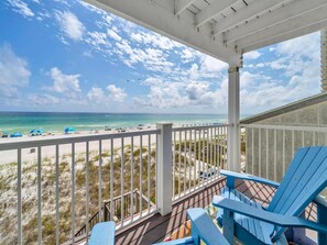 A beach view from a covered deck with blue chairs, a railing, and a view of the ocean and beach. - Sunset Sanctuary (Panama City Beach)