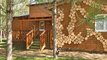 Una baita di legno con una scala che conduce a un patio, circondata da alberi.