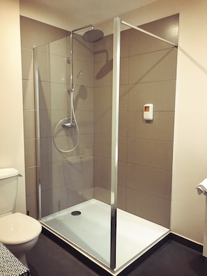 Een douchecabine met glazen wanden, een handdouche en een bedieningspaneel aan de muur.