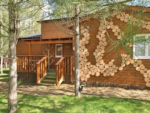 A wooden cabin with a staircase leading to a deck, surrounded by trees. - Défiplanet' (Dienne)