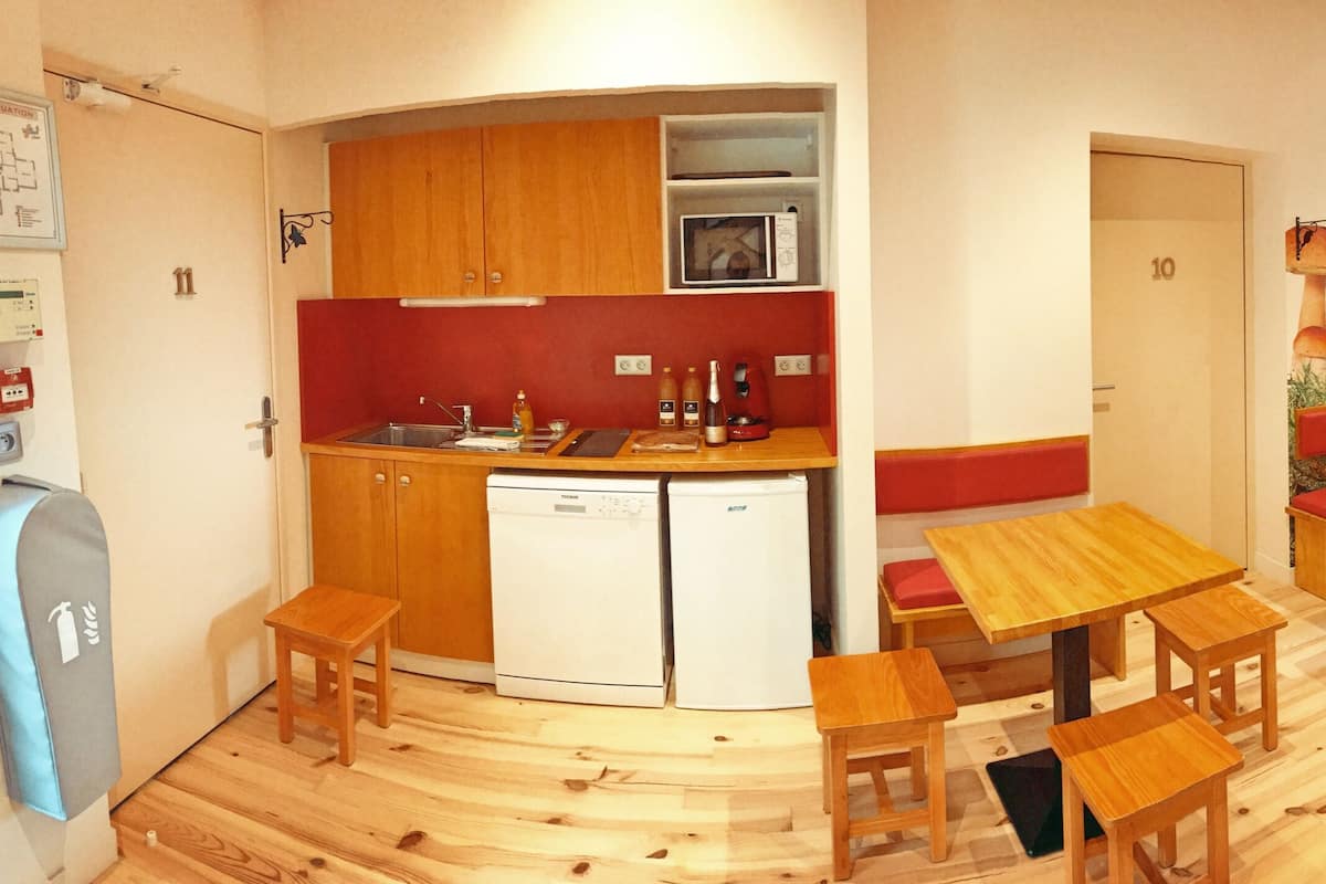 A compact kitchen with wooden cabinets and a microwave, a dining area with wooden tables and red cushioned benches, and a wall with a mushroom mural.