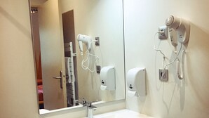 A bathroom with a white vanity, a mirror, a hairdryer, and a towel dispenser. - Défiplanet' (Dienne)