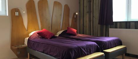 Un dormitorio con dos camas, cabeceros de madera, una ventana con cortinas y suelo de madera.