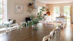 A modern kitchen with white cabinetry, a wooden dining table, and a large window. - Silas House (Lexington)