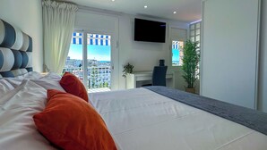 Een moderne slaapkamer met een groot bed, een bureau, een stoel, een televisie en een balkon met uitzicht op de stad.