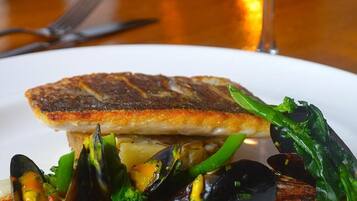 A plate of food with mussels, broccoli, and a piece of fish on a white plate.