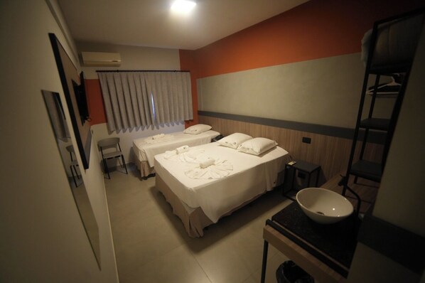 Quarto de hotel com duas camas, pia, espelho e janela com cortinas.