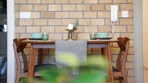 A dining area with a brick wall, a table with a patterned tablecloth, two chairs, a candle, and a telephone. - Nakheel Residence by House living (Sabah Al Salem)