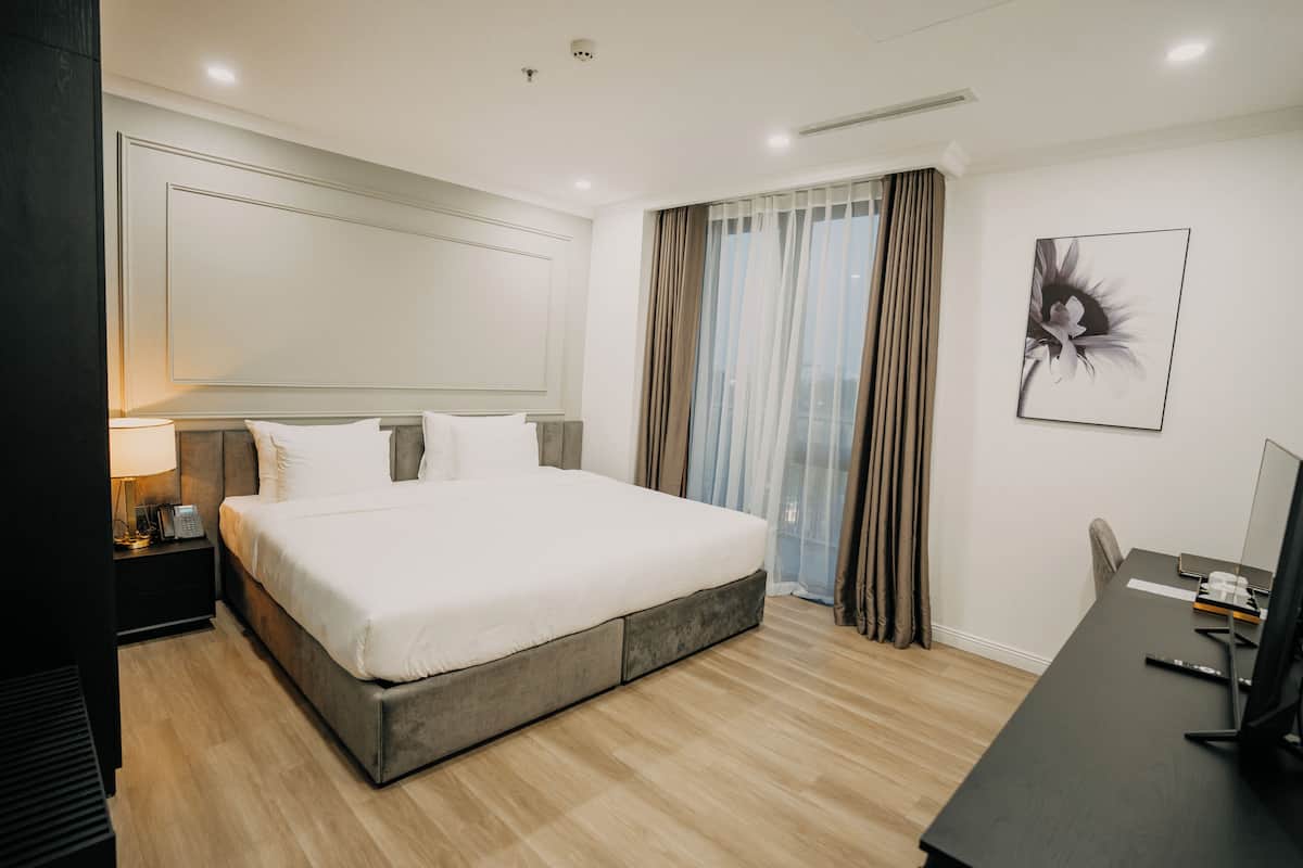 Una habitación de hotel moderna con una cama grande, un escritorio con computadora y una ventana con cortinas.