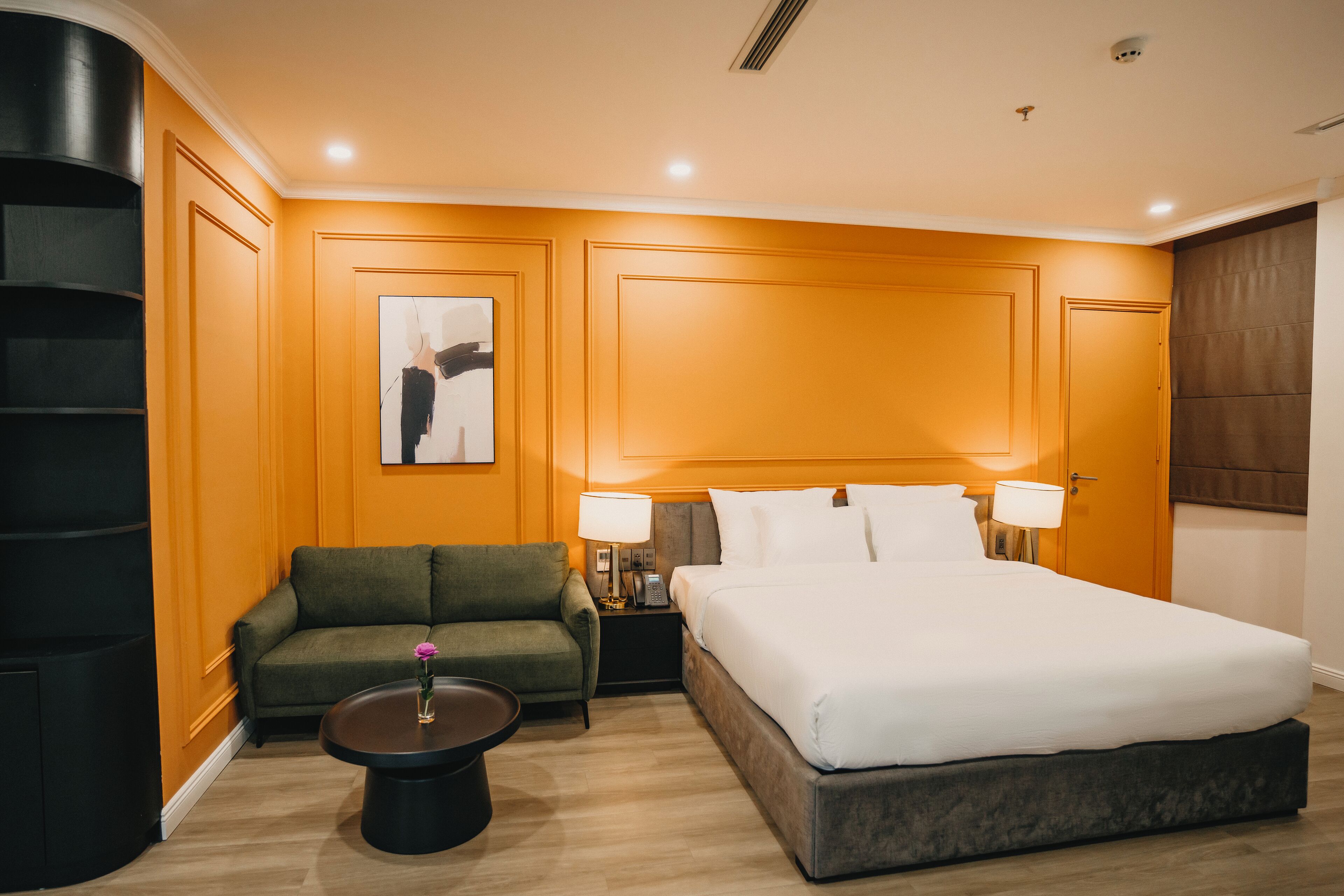 Een hotelkamer met een groot bed, een groene bank, een kleine tafel met een vaas en een kunstwerk aan de wand.