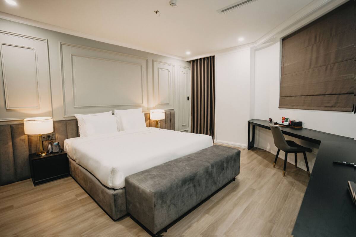 Una habitación de hotel moderna con una cama grande, lámparas de noche, un escritorio y una silla.