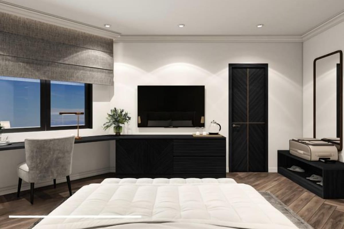 A modern bedroom with a large bed, a desk with a chair, a TV, and a wardrobe.