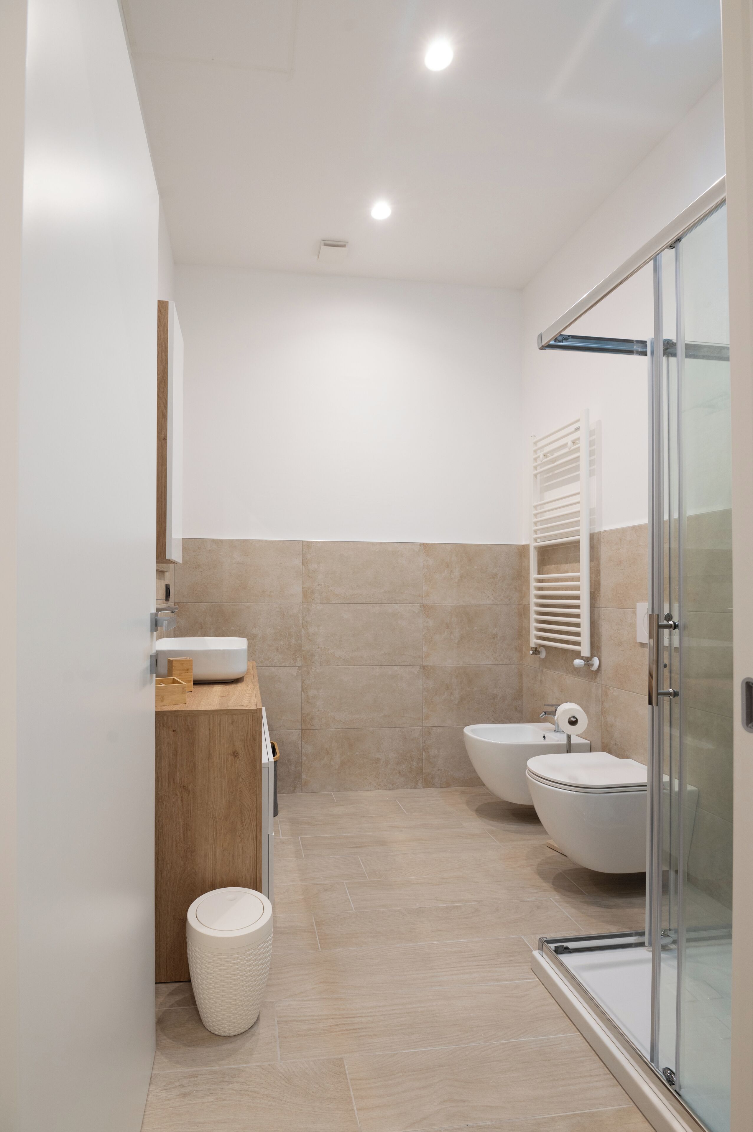 A modern bathroom with a wooden vanity, a glass shower enclosure, and a white sink.